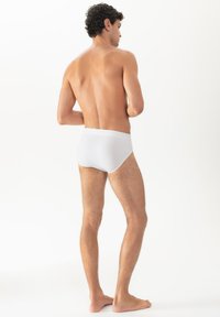 Witte slip met een gladde textuur en elastische tailleband, getoond op een persoon van achteren, waarbij de pasvorm en snit worden benadrukt.