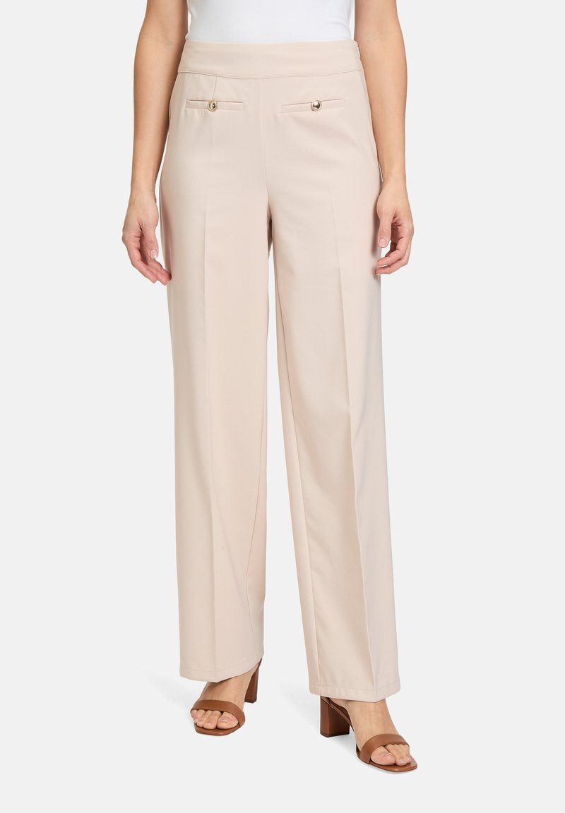 Pantalons beige à jambes larges avec une texture lisse, comportant deux poches avant et des accents de boutons dorés. Associés à des sandales à talons bruns.