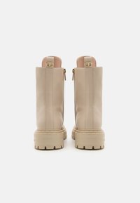 Bottes chelsea en cuir beige avec une finition texturée, présentant une semelle épaisse et des accents dorés, vues de l'arrière avec des zips.