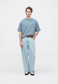 Gaiši zils kokvilnas T-krekls, kas saskaņots ar gaiši ziliem džinsiem. Ievērojama plata kāju forma un brūns ādas josta. Melni un balti apavi noslēdz izskatu.