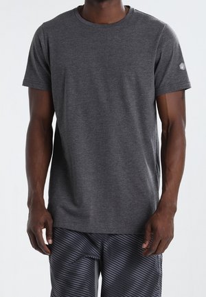 Homme portant un t-shirt uni à manches courtes gris foncé et un short rayé noir et gris, debout devant un fond uni.