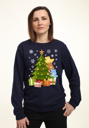 Mørkeblå sweatshirt med et dekoreret juletræ, der har tre tøjdyr og farverige gaver. Snefnugmønstre omgiver designet.