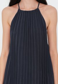 Abito plissettato blu con scollo a halter, realizzato in un tessuto morbido. Caratterizzato da pieghe verticali e una vestibilità comoda. Le spalline sono sottili e regolabili.