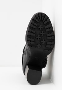 Zapato de cuero negro con una suela de goma negra texturizada que presenta un patrón de agarre, en ángulo sobre un fondo blanco.