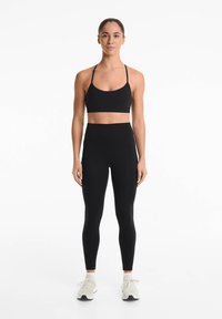 Zwarte sportbeha met dunne banden en zwarte high-waisted leggings. Soepele textuur, rekbare stof, gecombineerd met lichte sneakers.