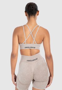 Sujetador deportivo beige y pantalones cortos de talle alto con tela texturizada, que presentan tirantes cruzados en la espalda y un logo en la cintura.