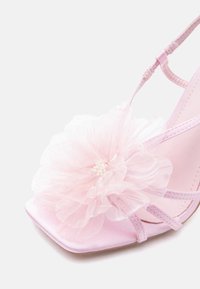 Ροζ σατέν ψηλοτάκουνο σανδάλι με λεπτές τιράντες και μεγάλο διάφανο υφασμάτινο λουλούδι με μικρό λευκό χάντρα στο κέντρο στην περιοχή των δαχτύλων του ποδιού.