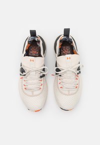 Buty sportowe z siateczkową cholewką w kolorze beżowym, z czarnymi akcentami i pomarańczowymi detalami. Posiadają amortyzowaną podeszwę i płaskie sznurowadła.