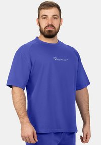 T-shirt bleu à manches courtes avec col rond et logo brodé sur le devant. Le tissu semble lisse avec une coupe décontractée.