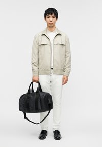 Μαύρη σακ βουαγιάζ με μοτίβα, διπλές λαβές στο πάνω μέρος, αποσπώμενο ιμάντα ώμου, λεία υφή και διακριτική σήμανση. Μέγεθος και σχήμα για ευέλικτη χρήση.