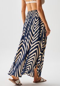 Falda maxi con cintura fruncida, con fondo azul marino y patrones de zigzag en crema, y una abertura lateral, confeccionada en tela ligera.