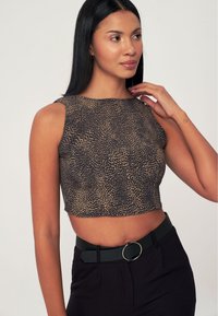 Crop top con stampa leopardata in beige e nero, con scollo a giro e senza maniche. Indossato con pantaloni neri a vita alta e una cintura.