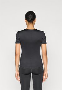 Μαύρο εφαρμοστό μπλουζάκι με κοντά μανίκια, λεία υφή, στρογγυλή λαιμόκοψη και ορατές λεπτομέρειες ραφής. Φοριέται με αντίστοιχο μαύρο κολάν.