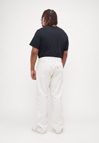 Pantalones de algodón blancos con un corte relajado, que cuentan con bolsillos traseros y un logotipo sutil. Combinados con una camiseta de cuello redondo negra.