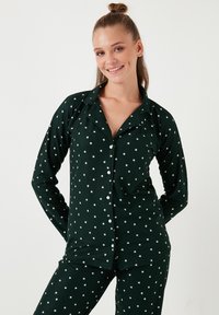 Ensemble de pyjama vert foncé composé d'un haut à boutons et d'un bas assorti, avec un motif d'étoiles blanches sur l'ensemble. Tissu doux et extensible.
