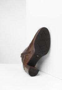 Bruine leren enkelboot met een ritssluiting, gestructureerde hak en patroon op de zool. Voorzien van een ronde neus en een minimalistisch ontwerp.