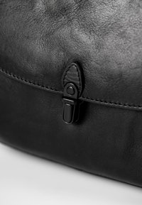 Borsa in pelle nera con una superficie liscia, dotata di una chiusura a scatto nera prominente e cuciture lungo il bordo per garantire durata.