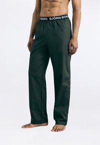 Calças largas de cor verde-escuras com um cós elástico preto com o logótipo "BJÖRN BORG". Textura suave e um corte descontraído.