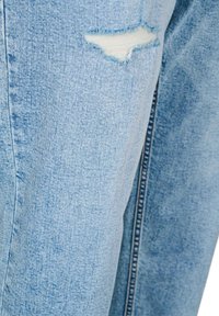 Light blue denim jeans showing a small horizontal rip near the upper thigh with white threads visible beneath.