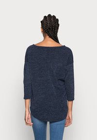 Top de manga larga azul marino, texturizado, con un escote amplio y hombros caídos, que presenta un dobladillo curvado y un corte relajado.