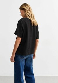 Zwarte textuur short-sleeve top met een losse pasvorm, gecombineerd met high-waisted blauwe denim jeans, gezien van achteren.