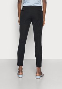 Pantalon noir ajusté avec une texture lisse, comprenant deux poches arrière et une silhouette droite. Complété par des sandales à talons bleu clair.