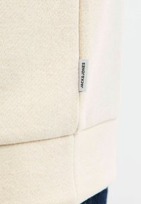 Krämfärgad sweatshirt med en strukturerad stickad yta och en etikett med texten "JACK & JONES" på sidan. Har en slät fåll och ärmar.