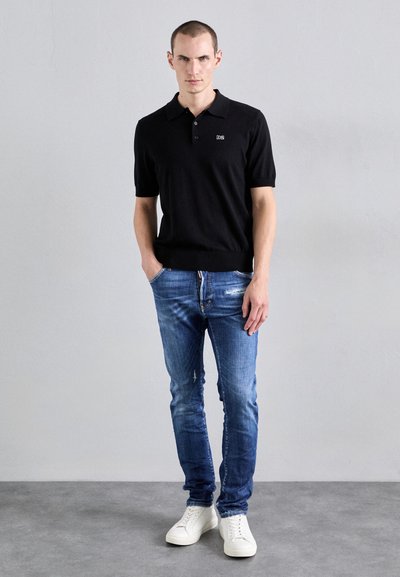 Zwarte polo met korte mouwen en knopen, gecombineerd met blauwe versleten jeans en witte sneakers. Casual pasvorm, soepele textuur en minimalistisch ontwerp.