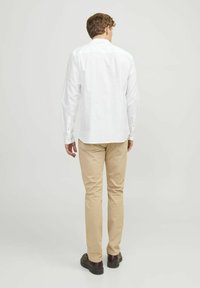 Hvid langærmet skjorte med krave, der kan knappes ned, parret med lyse beige bukser og mørke sko. Skjorten har et enkelt design og lige snit.
