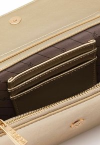 Beige Kunstlederwallet mit goldenen Details, mehreren Kartenfächern und Reißverschluss. Innenausstattung mit gemusterter Fütterung. Außenseite mit Druckverschluss.