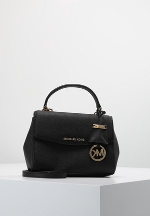 Sort Michael Kors håndtaske med top-håndtag, klaplukning, aftagelig skulderrem og rund guldfarvet logo-vedhæng, vist på en hvid overflade.