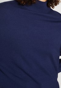 Marinblå, lätt turtlenecktröja gjord av mjukt material, med ribbat halsband och slät yta, med en sömlös design.