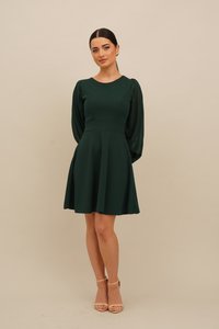 Grønn, vid kjole med tettsittende liv, gjennomsiktige lange ermer og rund halslinning. Jevn tekstur med en klassisk silhuett og lekende bevegelse.