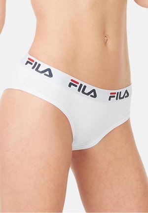 Gros plan sur une personne portant un slip blanc avec une ceinture blanche arborant le logo FILA en lettres noires et rouges.