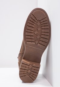 Brown leather shoe with a textured rubber sole. Sole features a tread pattern with cross shapes and size 37 marked on the bottom.