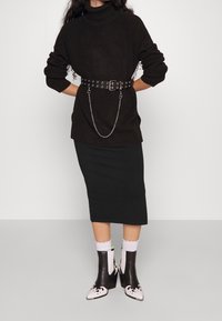 Svart stickad polotröja med ett silverfärgat kedjebälte, ihop med en svart knälång pennkjol och svarta ankelboots med blommönster.