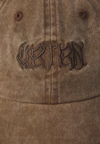 Brown fabric cap with an embossed dark brown logo. Material features a textured finish and structured design, including a stitched vent and peak.