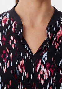 Blusa de tejido negro con un sutil patrón floral en rojo, rosa y azul. Escote en V con cuello, textura suave, de peso medio.