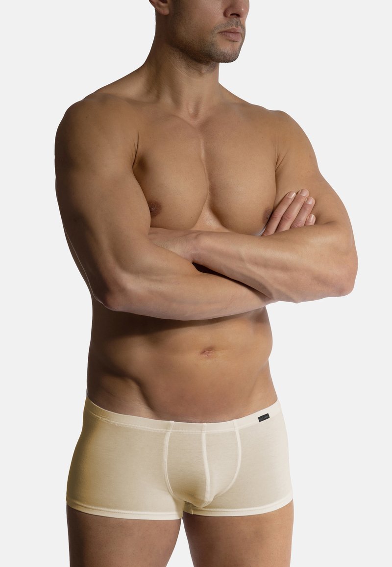 Béžové bavlněné boxerky s měkkou texturou, s kontrastním pasem a těsným střihem, vystavené na modelce se založenýma rukama.