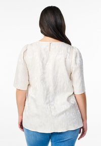 Kermanen, tekstuuri t blouse lyhyillä puffihihnoilla ja takanapituksella, jossa on hienovarainen kukkakuosi. Yhdistetty sinisiin farkkuihin.