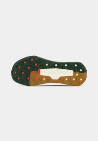 Green and brown outsole with prominent grip patterns, red and white accents, and "NIKE" branding on a light-colored midsole.