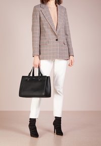 Czarna skórzana torebka z podwójnymi uchwytami, fakturowanym wykończeniem i błyszczącymi okuciami, noszona z kratkowaną marynarką, białymi dżinsami i czarnymi botkami na obcasie.