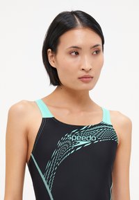 Μαύρο μαγιό με ανοιχτό τιρκουάζ ιμάντες και λεπτομέρειες. Διαθέτει δυναμικό μοτίβο και λογότυπο "speedo" στο στήθος. Κατασκευασμένο από ελαστικό υλικό.