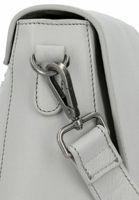 Primo piano di una chiusura in metallo argento che attacca una cinturino in pelle bianca al lato di una borsa in pelle bianca.