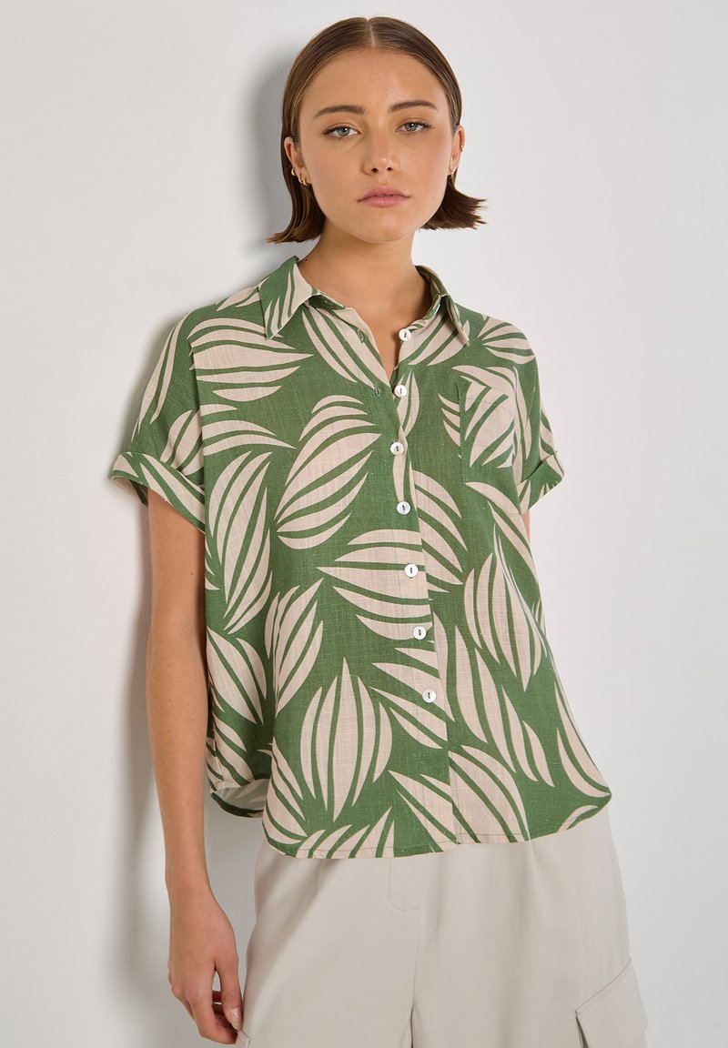 Camicetta verde a maniche corte con motivo di foglie beige, chiusura a bottoni sul davanti, colletto e vestibilità rilassata. Realizzata in tessuto leggero.