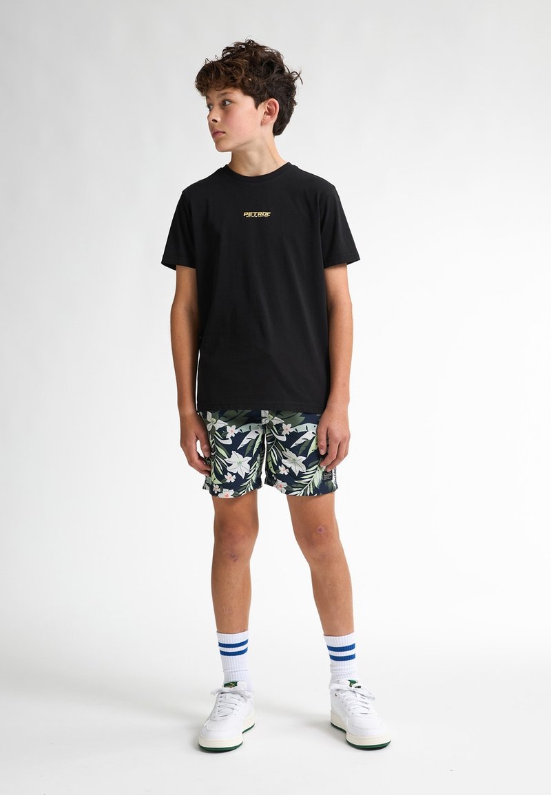 Zwarte katoenen T-shirt met gouden logo, bloemenpatroon shorts in groen en wit, witte sneakers en blauw gestreepte sokken.