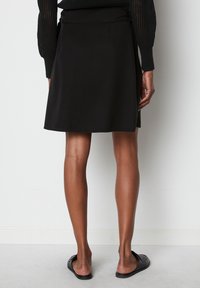 Sort skater-nederdel lavet af glat stof, med en tætsiddende talje og et flydende design, der falder over knæet.