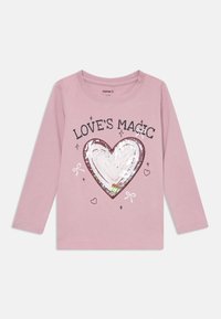 Camisa de manga longa rosa com um design de coração cintilante e o texto "A MAGIA DO AMOR", rodeado por pequenos corações e laços. Feita de algodão.