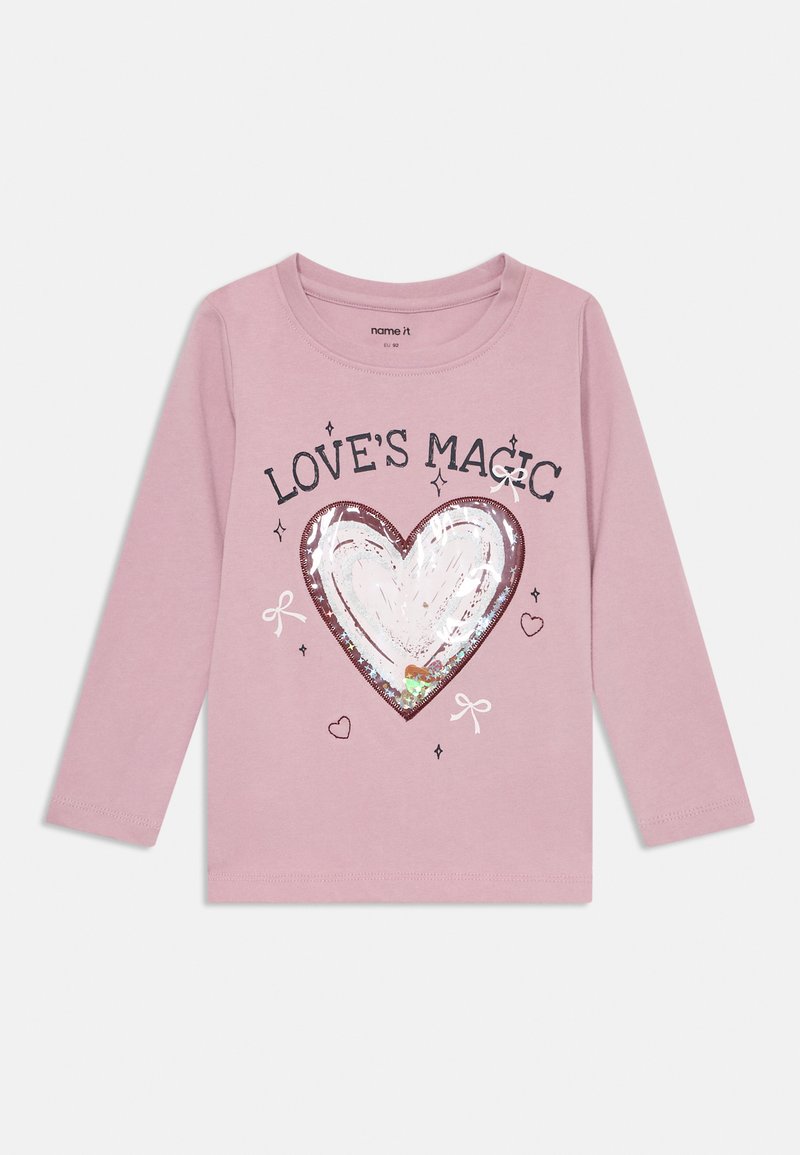 Camisa de manga longa rosa com um design de coração cintilante e o texto "A MAGIA DO AMOR", rodeado por pequenos corações e laços. Feita de algodão.