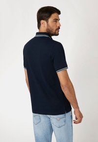 Marineblauwe polo met korte mouwen, voorzien van lichtblauwe boorden op de kraag en mouwen, gedragen met lichtblauwe spijkerbroeken.